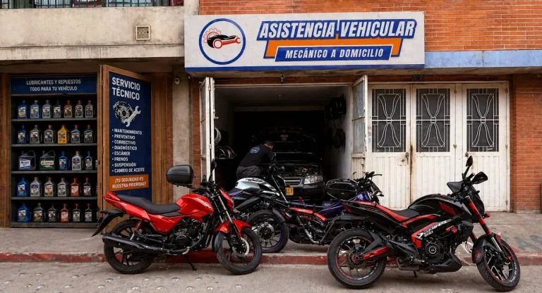 Fachada del local de Asistencia Vehicular en Fontibón, con el aviso del taller, estantería de lubricantes, motos parqueadas al frente y un técnico trabajando sobre un vehículo dentro del local.